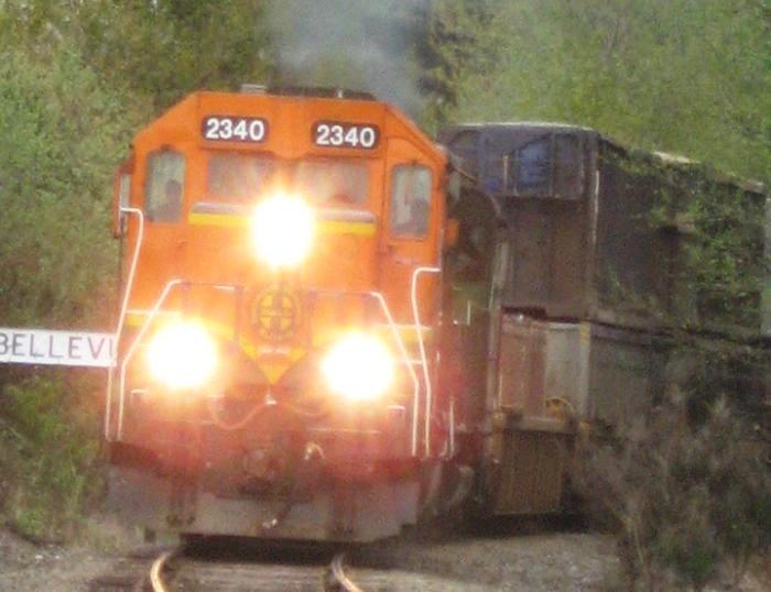 Diesel locomotive with three bright lights hauling train towards viewer